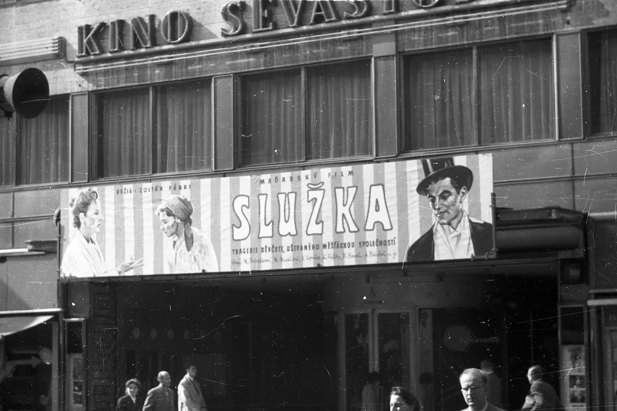 A black-and-white photograph of a cinema facade with the letters KINO SEVASTOPOL and a large film poster above the entrance, with people walking past below